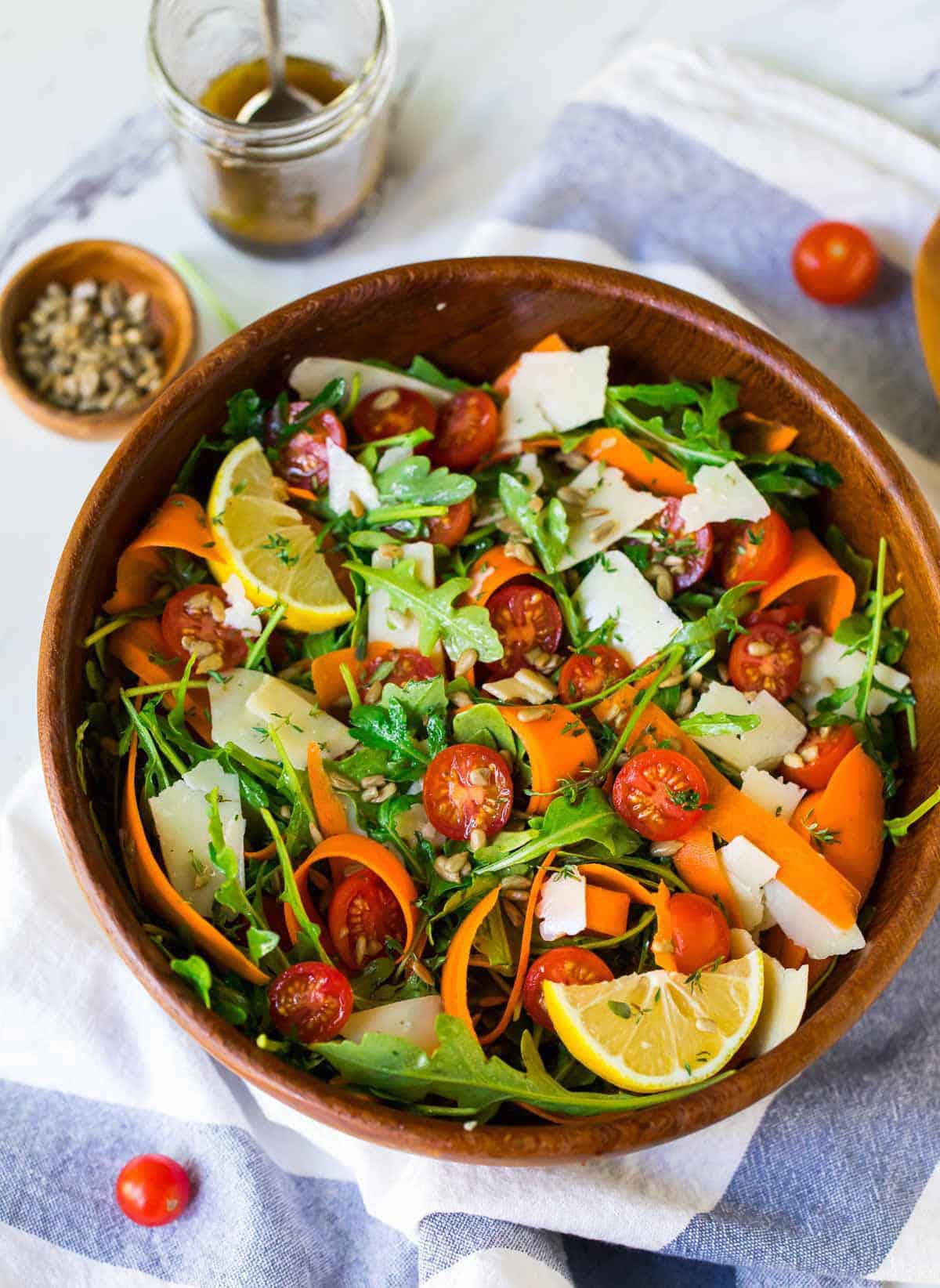 top down view of wooden bowl with an arugula salad, lemon, tomatoes, and sliced carrots.