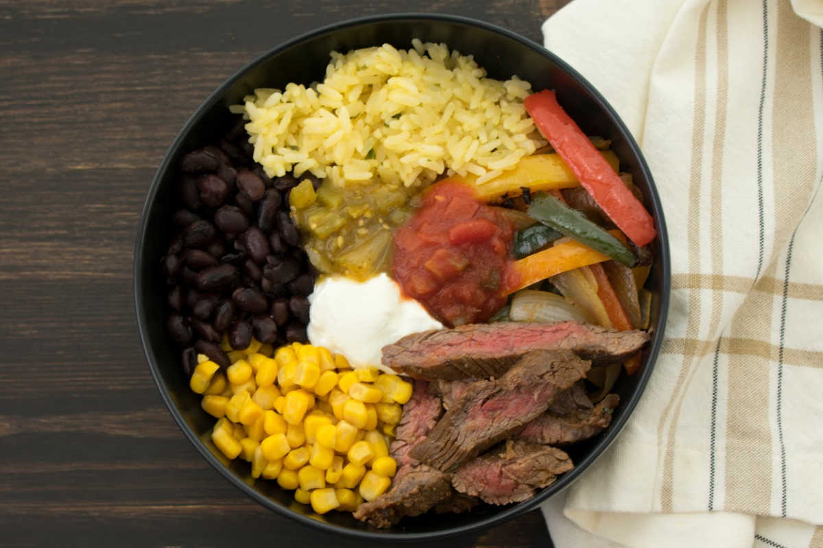 Presliced beef fajita strips in a bowl with corn, beans, peppers, and rice.