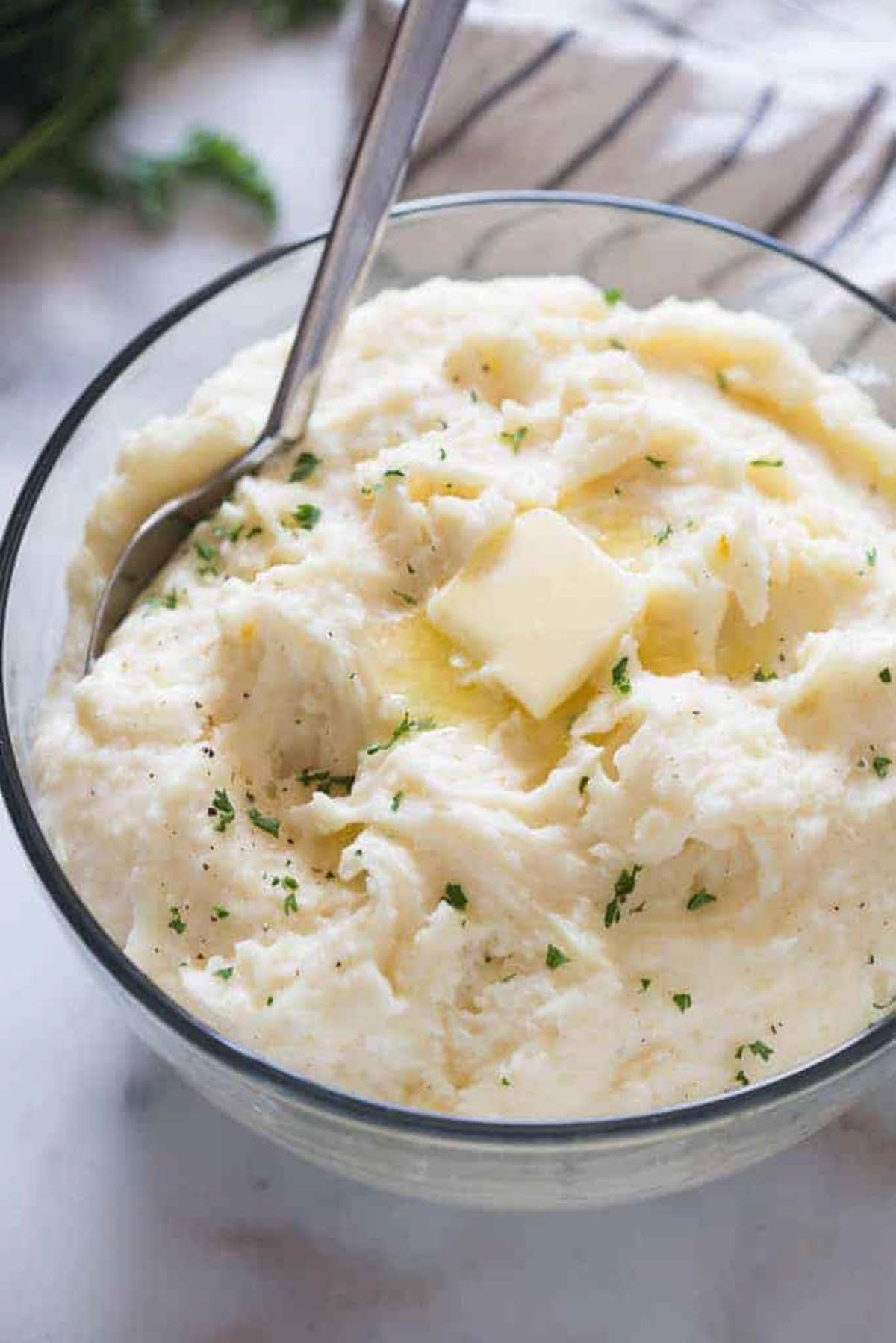 glass bowl with fluffy white mashed potatoes, butter and sprinkled with parsley.