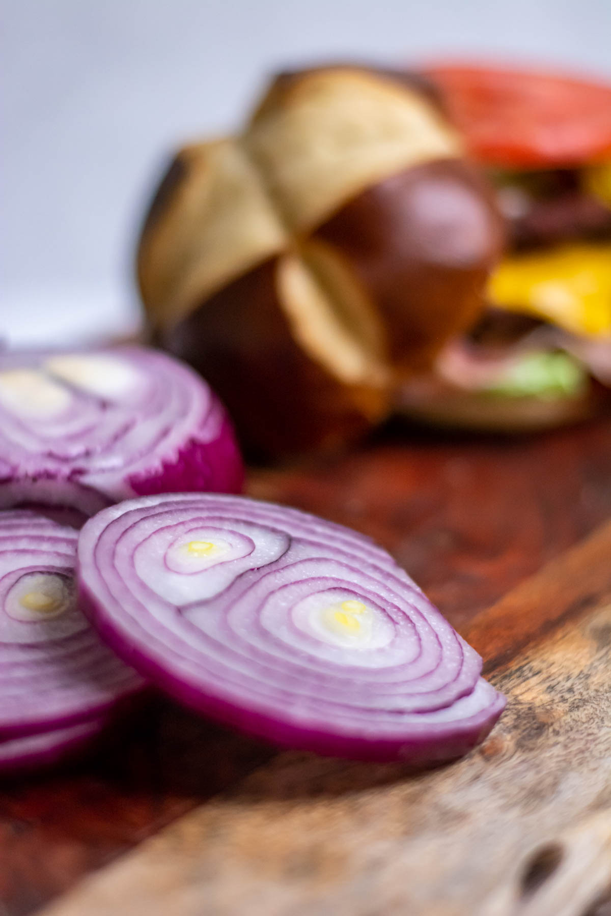 sliced red onions on a board with a burger in the background.
