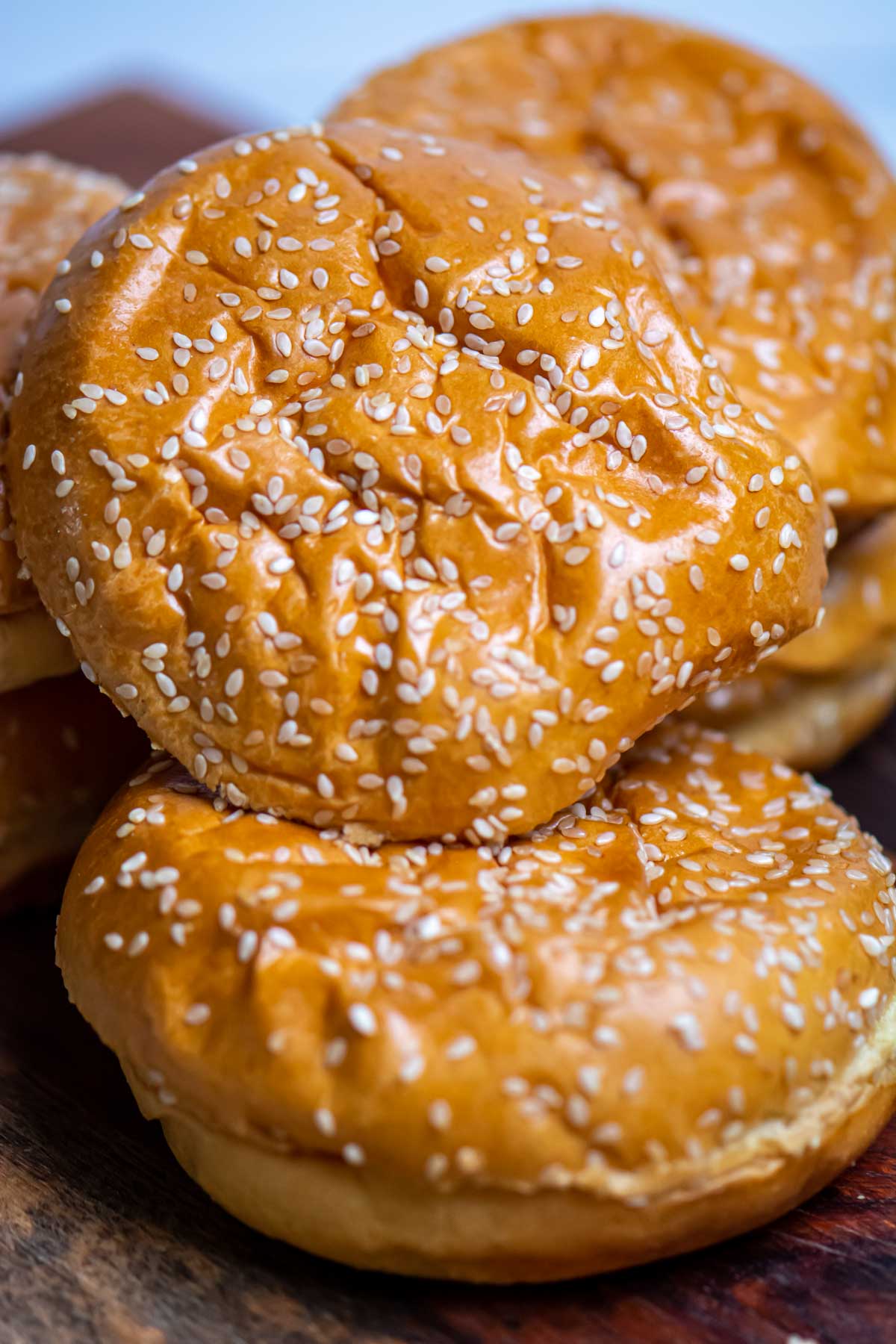 stack of sesame seed buns on a wooden cutting board.