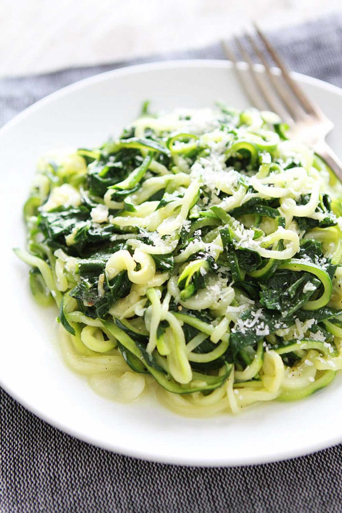 white plate filled with zucchini noodles, chopped spinach and topped with parmesan.