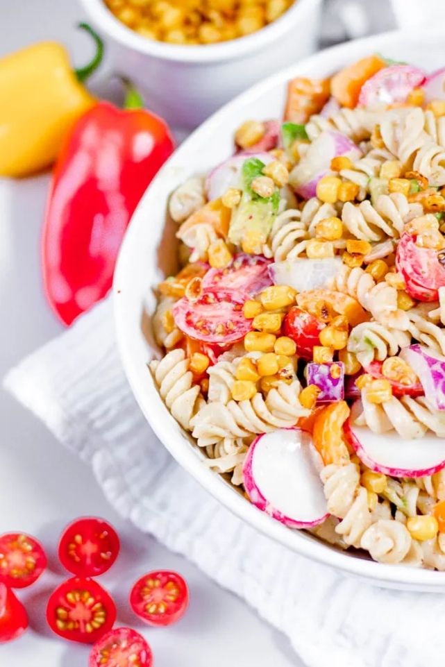 pasta salad in a white bowl with corn, tomatoes, onions and peppers.