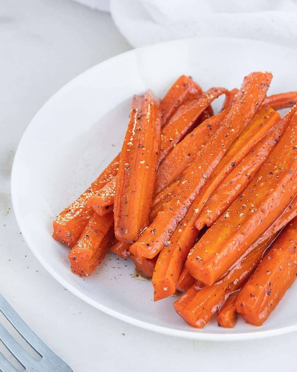 white bowl with long slices of glazed carrots topped with pepper.