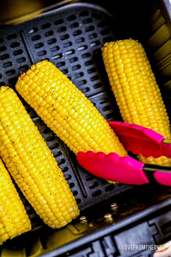 inside an air fryer basket with several whole corn on the cobs being cooked.