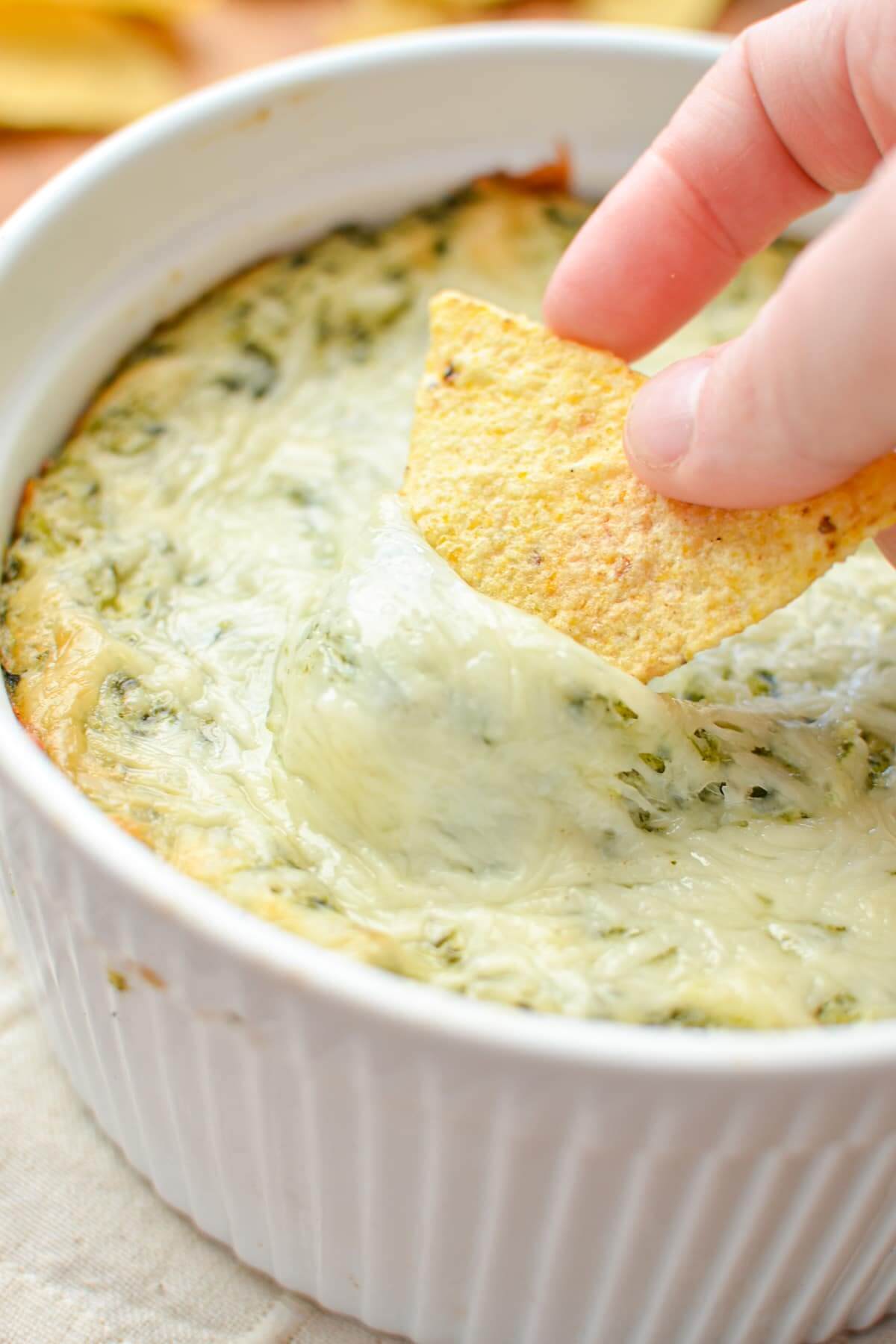 spinach and artichoke dip and a woman loading some on a corn chip.