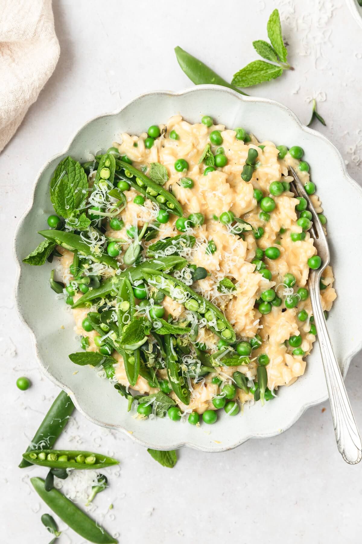 white scalloped bowl with risotto and fresh green peas and topped with shredded parmesan.