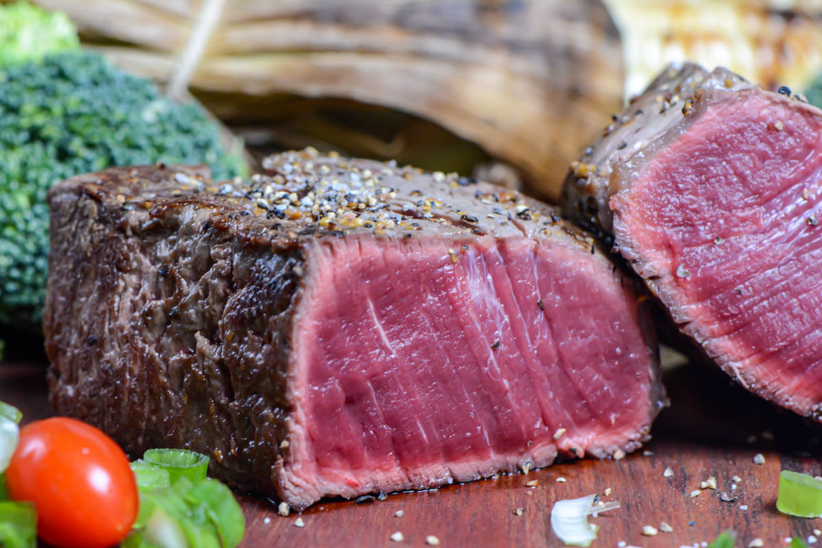 blue steak sliced in half with fresh vegetables on the wooden serving tray.