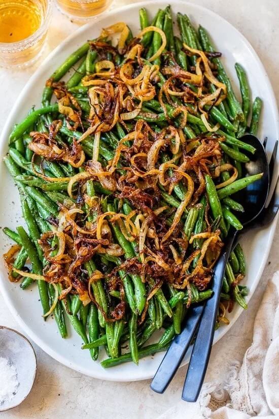top down view of a white plate loaded with green beans and topped with caramelized onions.