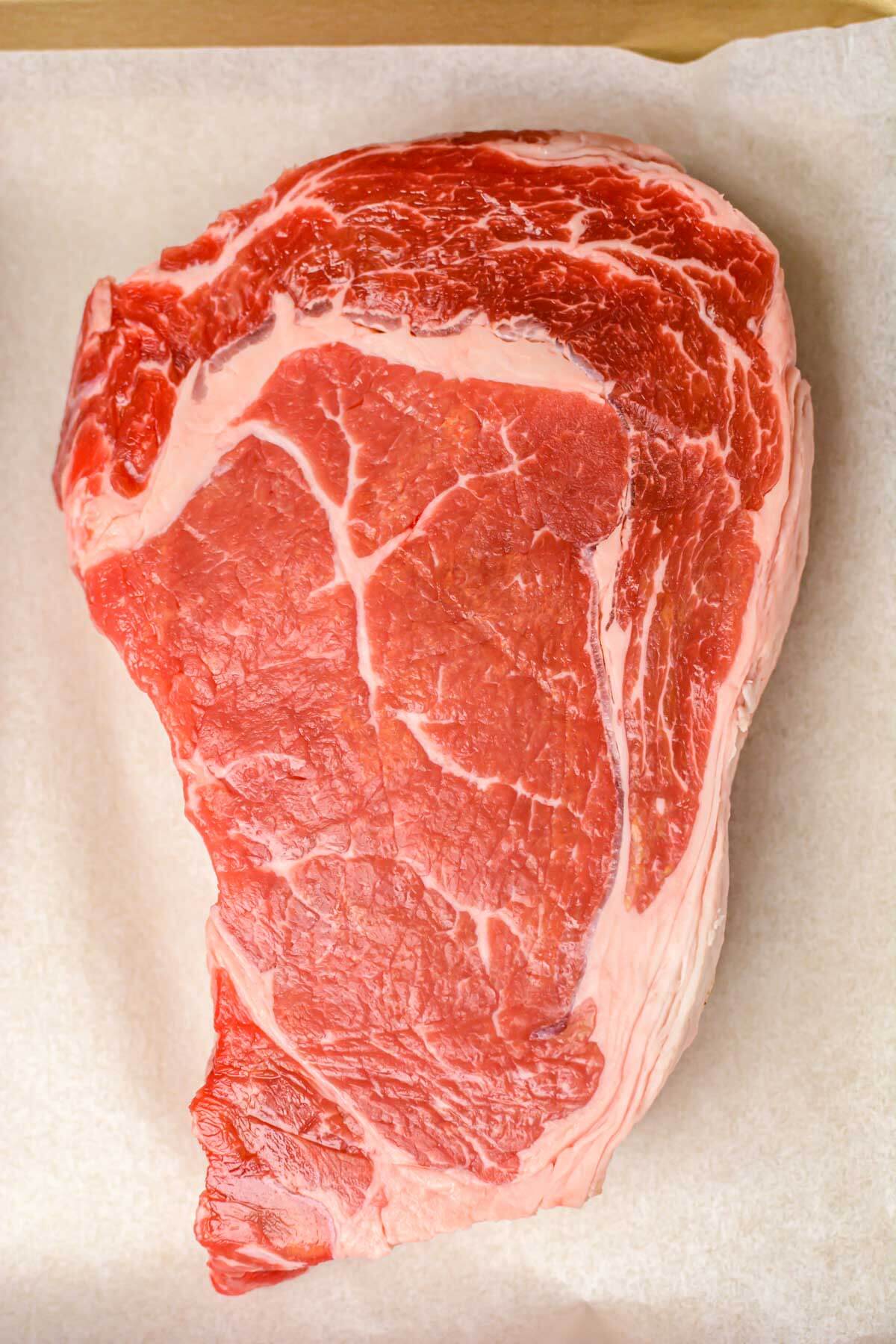 top down view of a ribeye steak on a lined sheet pan.