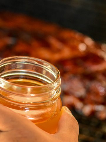 woman holding a jar of whiskey BBQ sauce over a batch of smoked ribs.