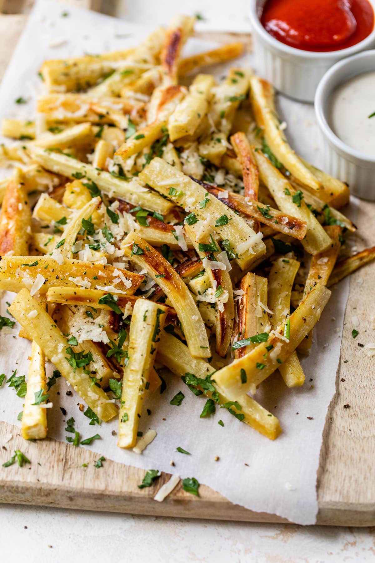 parsnip fries with herbs and spices on top with ketchup in the background.