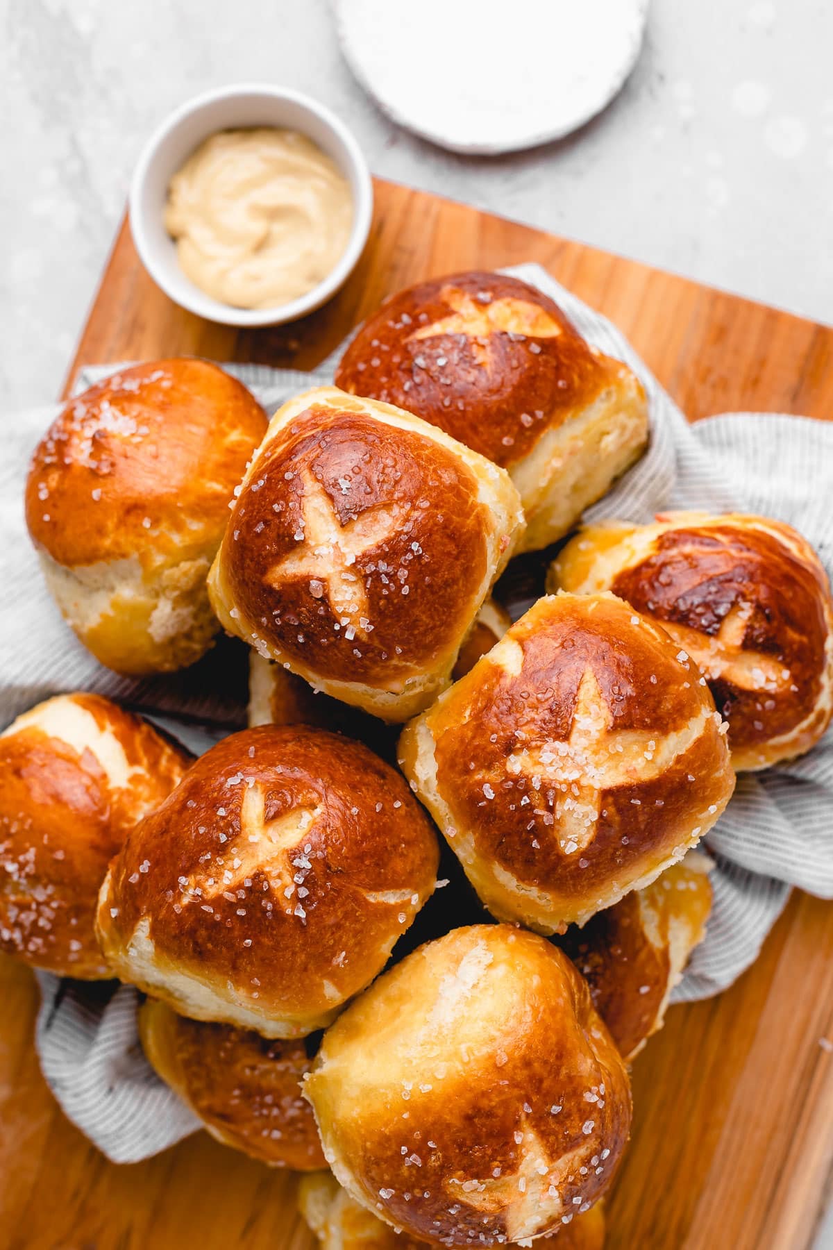 Pretzel-style buns stacked on a wooden cutting board.