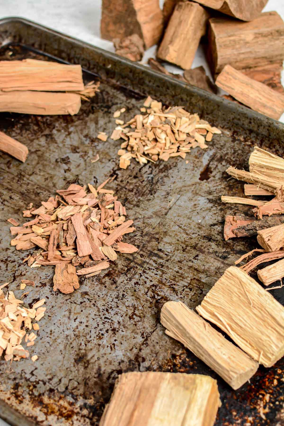 several piles of wood on a sheet pan from large chunks to finely ground chips.