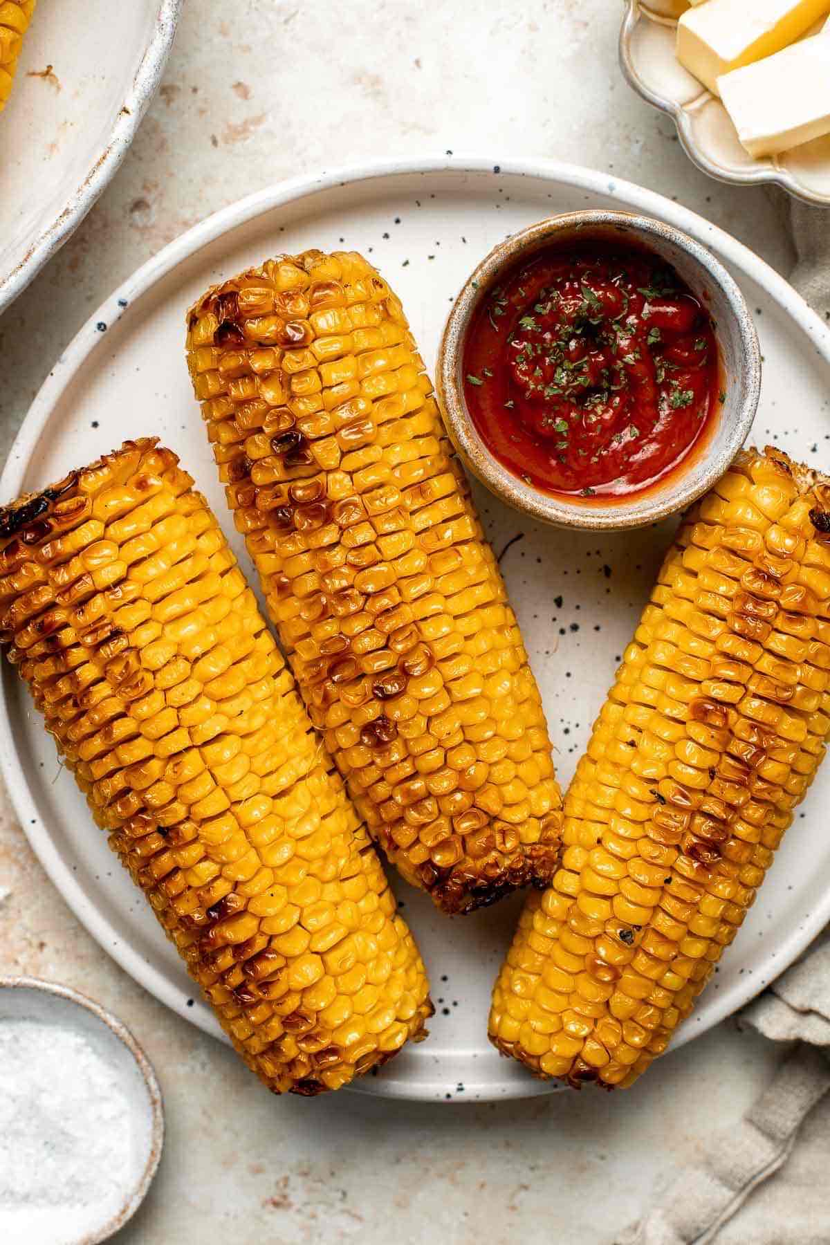 Oven roasted corn with tomato sauce on ceramic plate.