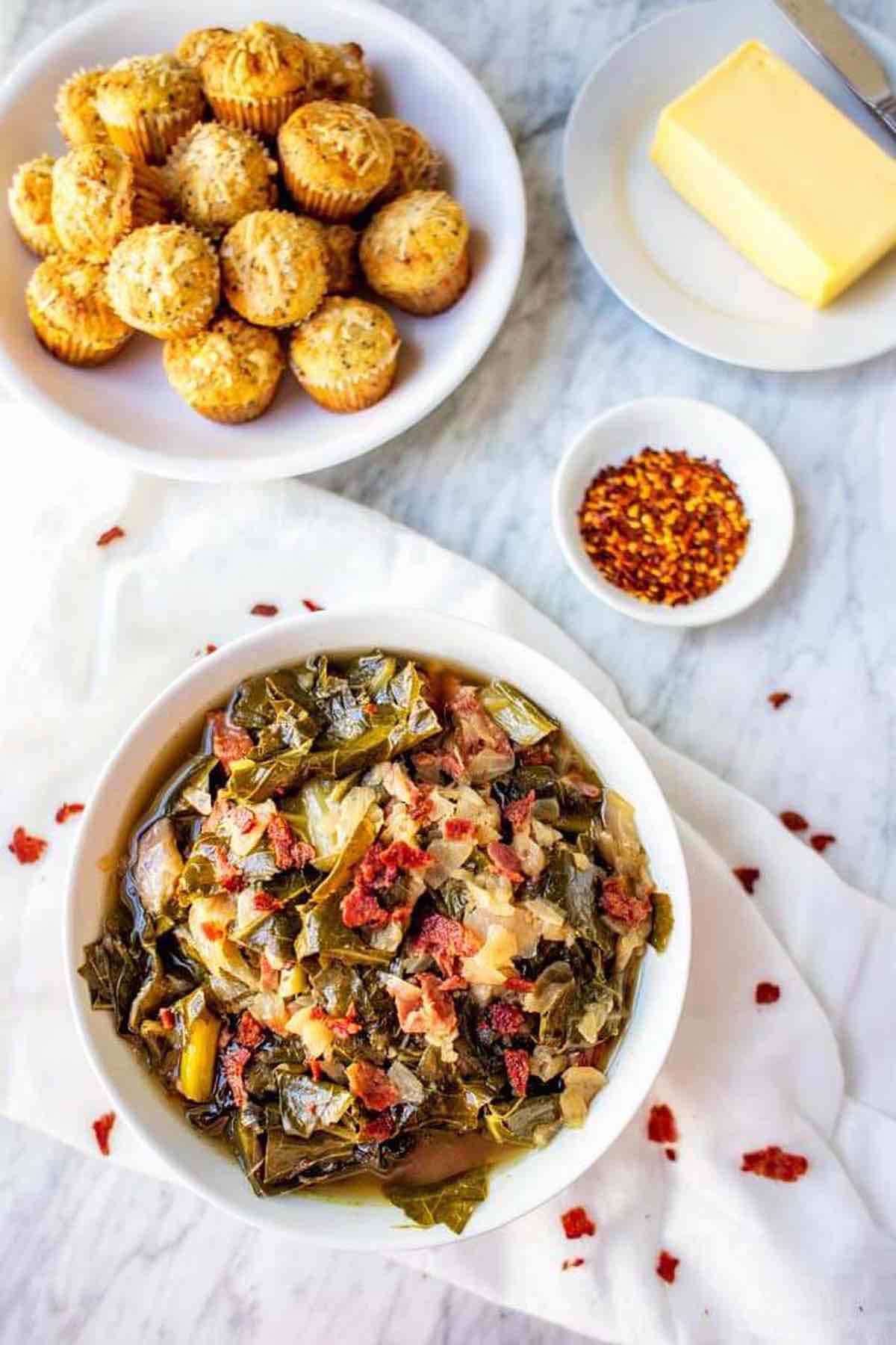 collard greens in a bowl with spices and muffins in the background.
