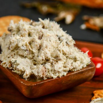 bowl of smoked fish dip on a serving platter with different crackers and fillets of smoked mackerel in the background.