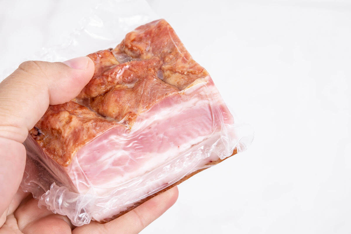 Raw slab bacon held in hand on white background.