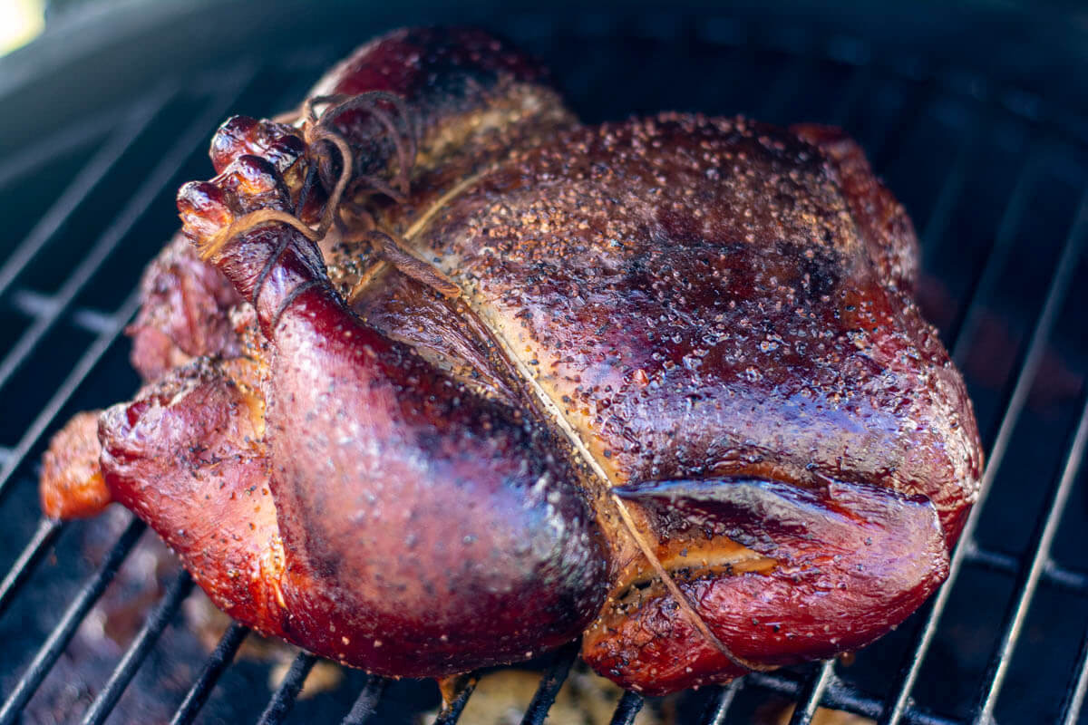 Smoked whole chicken with tied legs on the grill.