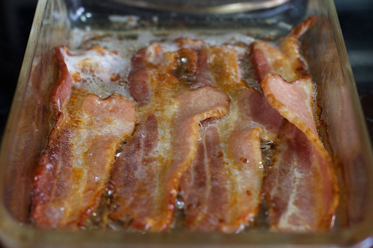 Undercooked overlapping slices of bacon in roasting pan.