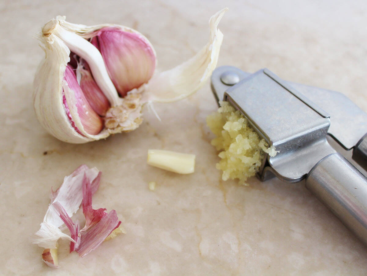 Crushed garlic in press and garlic head.
