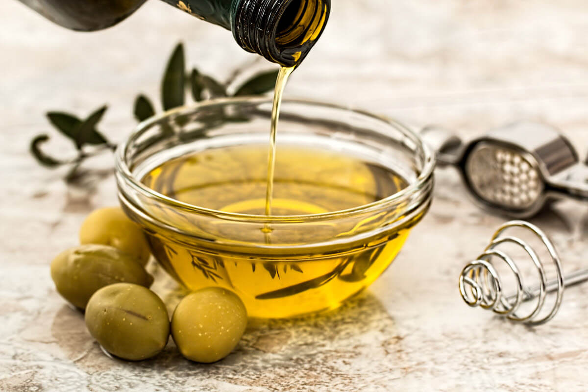 Olive oil poured in glass bowl with fresh green olives.