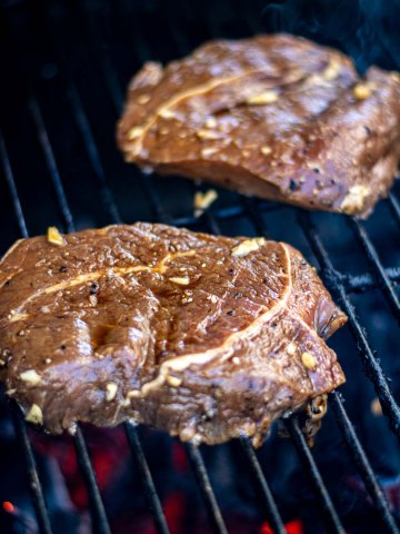 two grilled ranch steaks on direct heat over a charcoal grill grate.