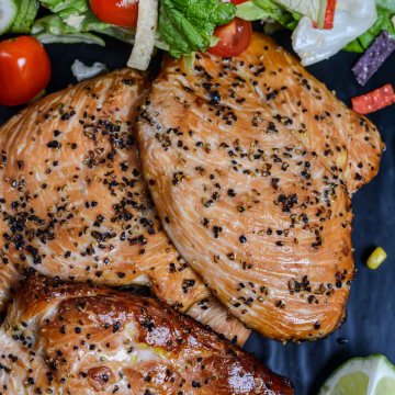 top down view of smoked chicken breasts on a black slate with a colorful salad and limes.