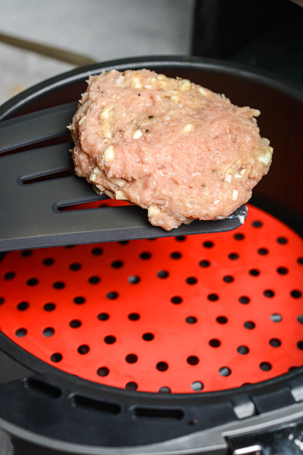 Raw turkey burger patty being placed in the Air Fryer.