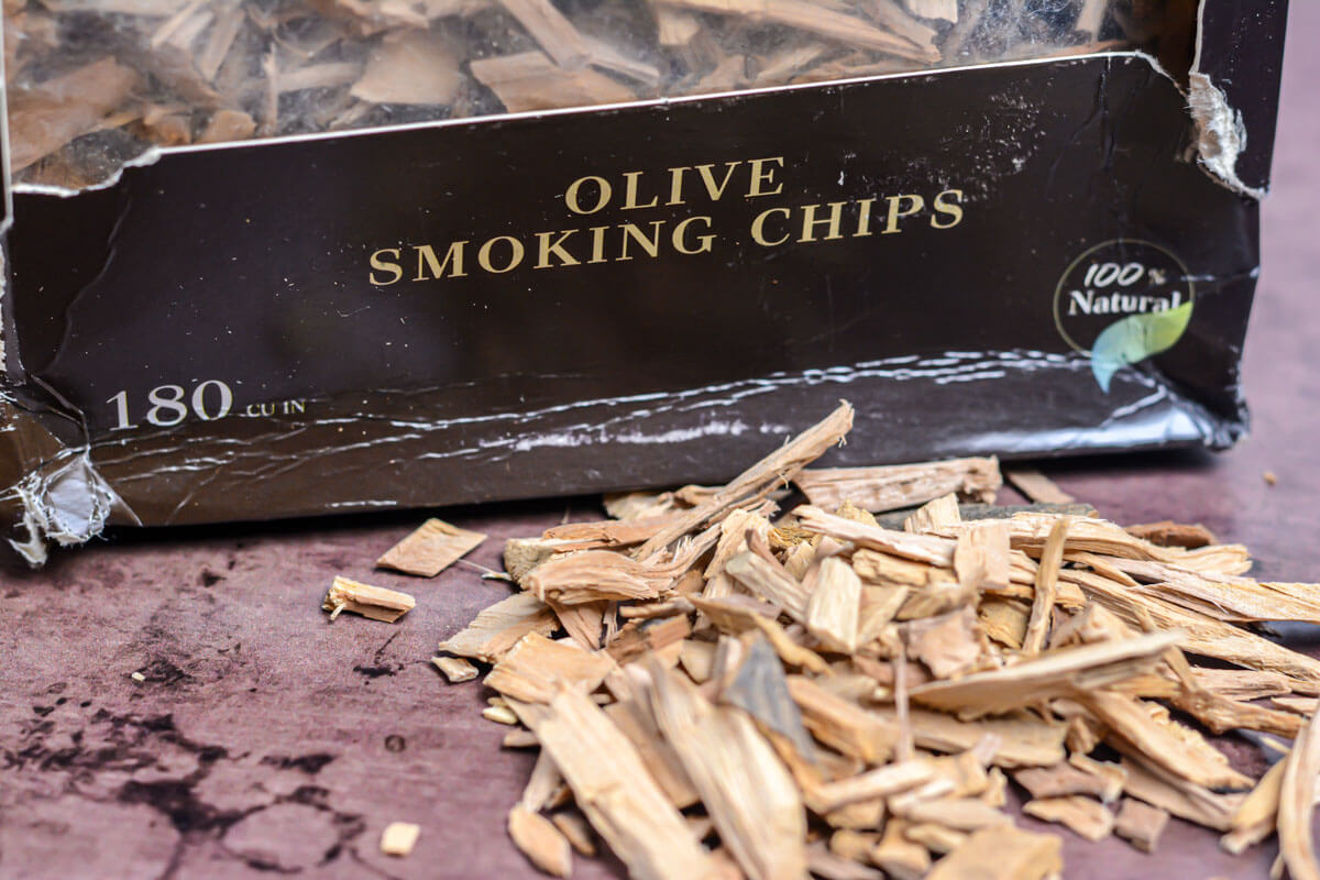 box of olive wood smoking chips and some in a pile in front.