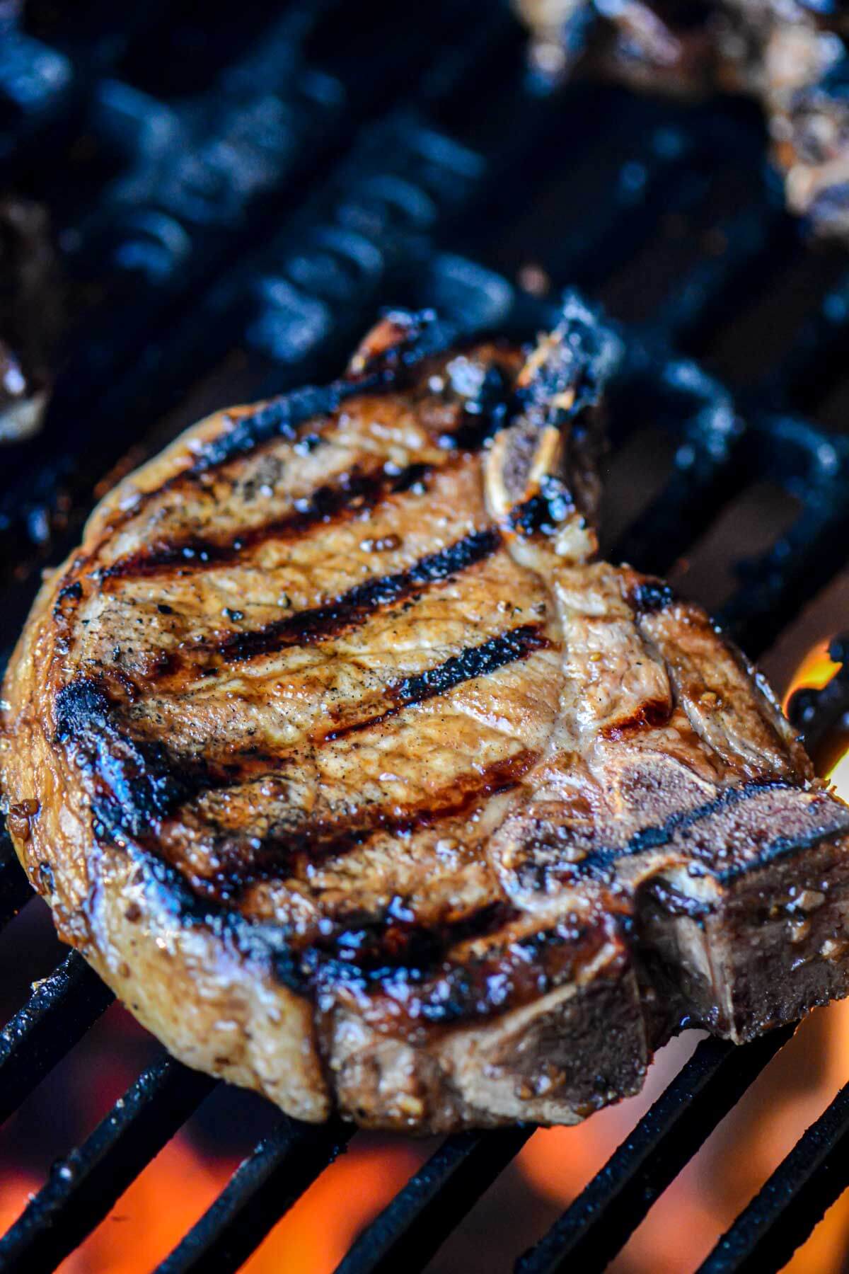 Large pork chop on the grill grate over orange charcoal and covered in a delicious pork marinade.
