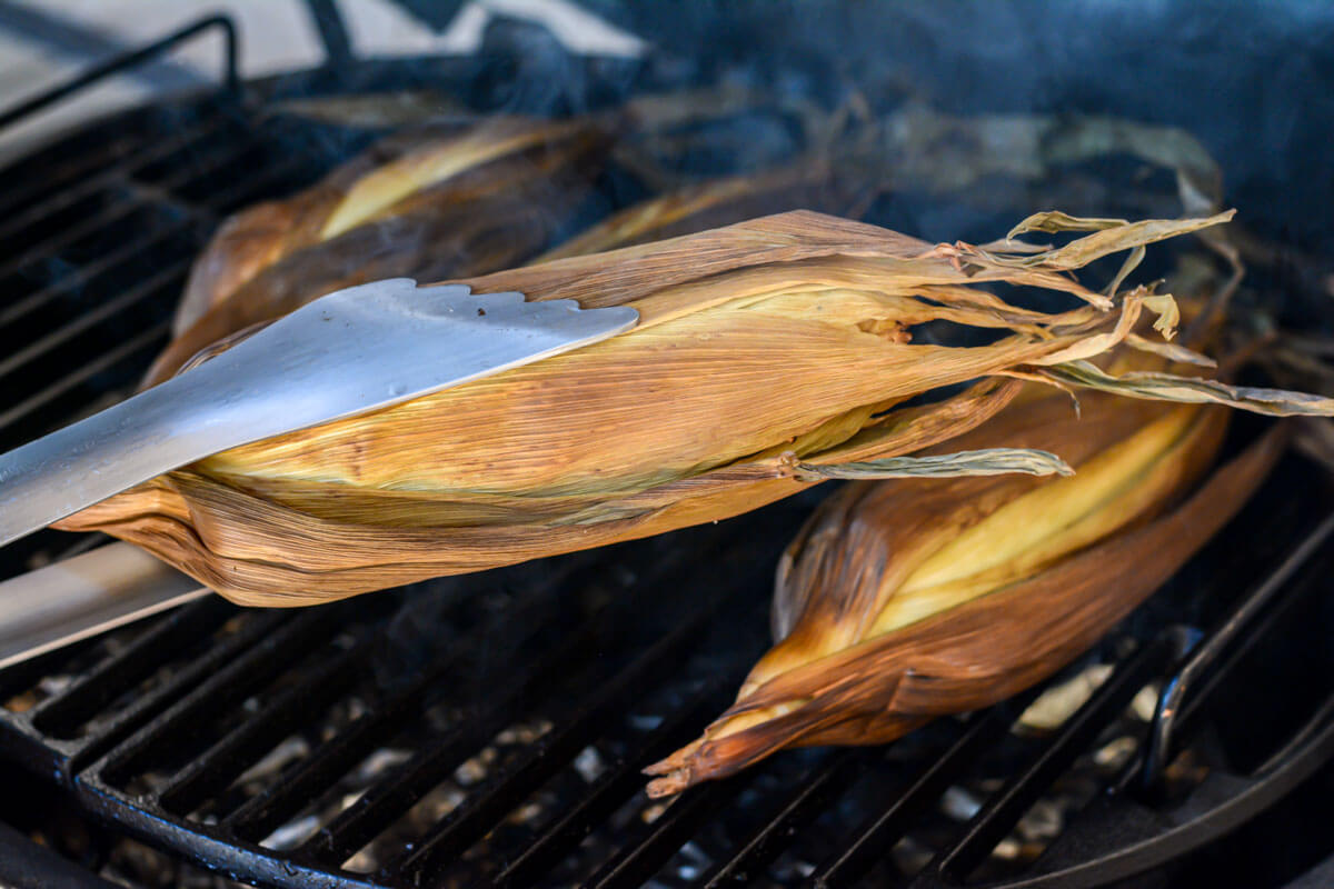 removing the smoked corn from the big green egg using BBQ tongs.