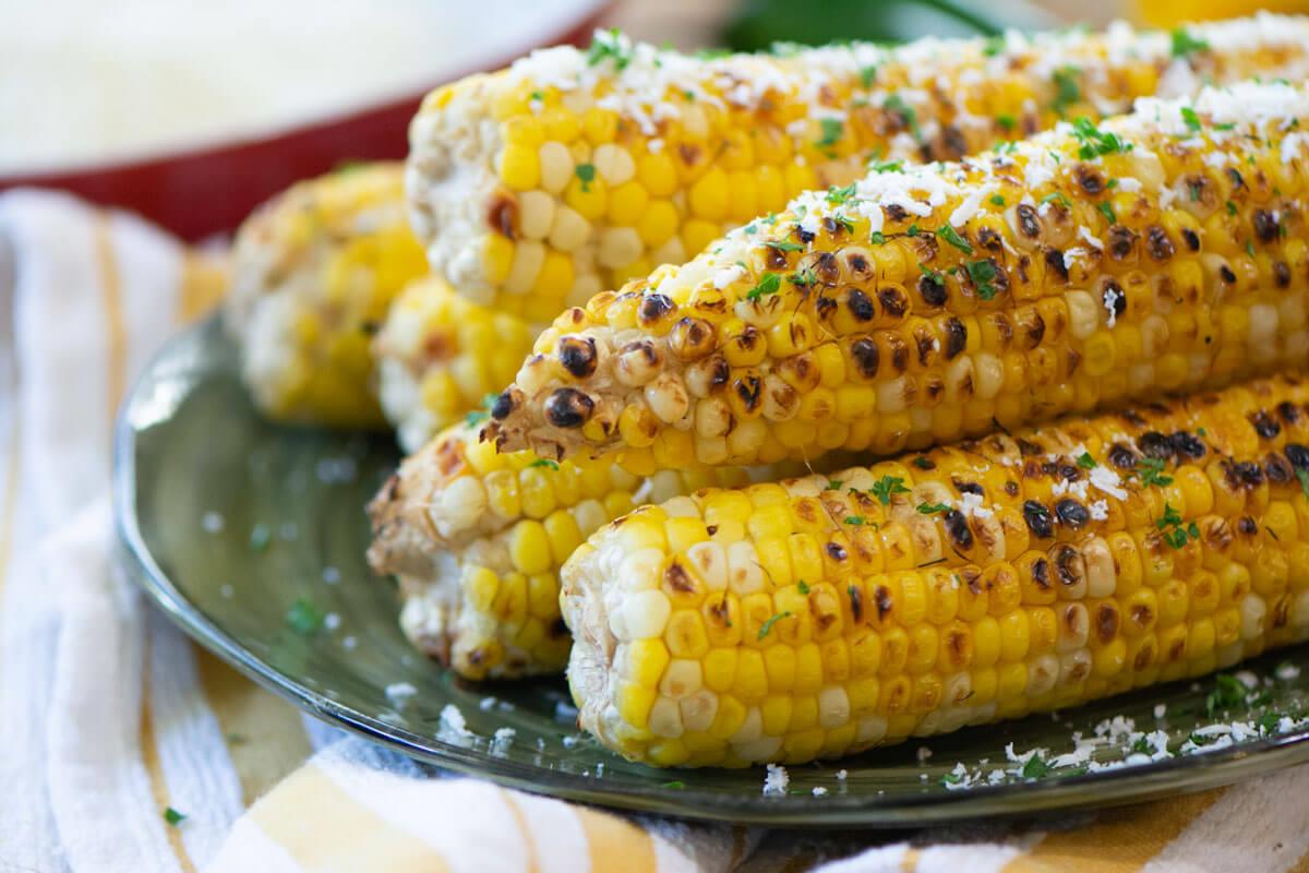 Side view of stacked grilled beer corn on green plate.