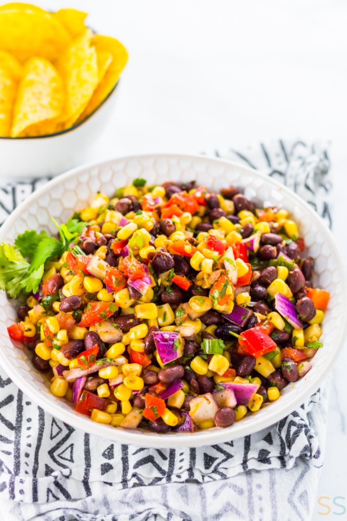 Black bean and corn salsa in white bowl on kitchen towel.