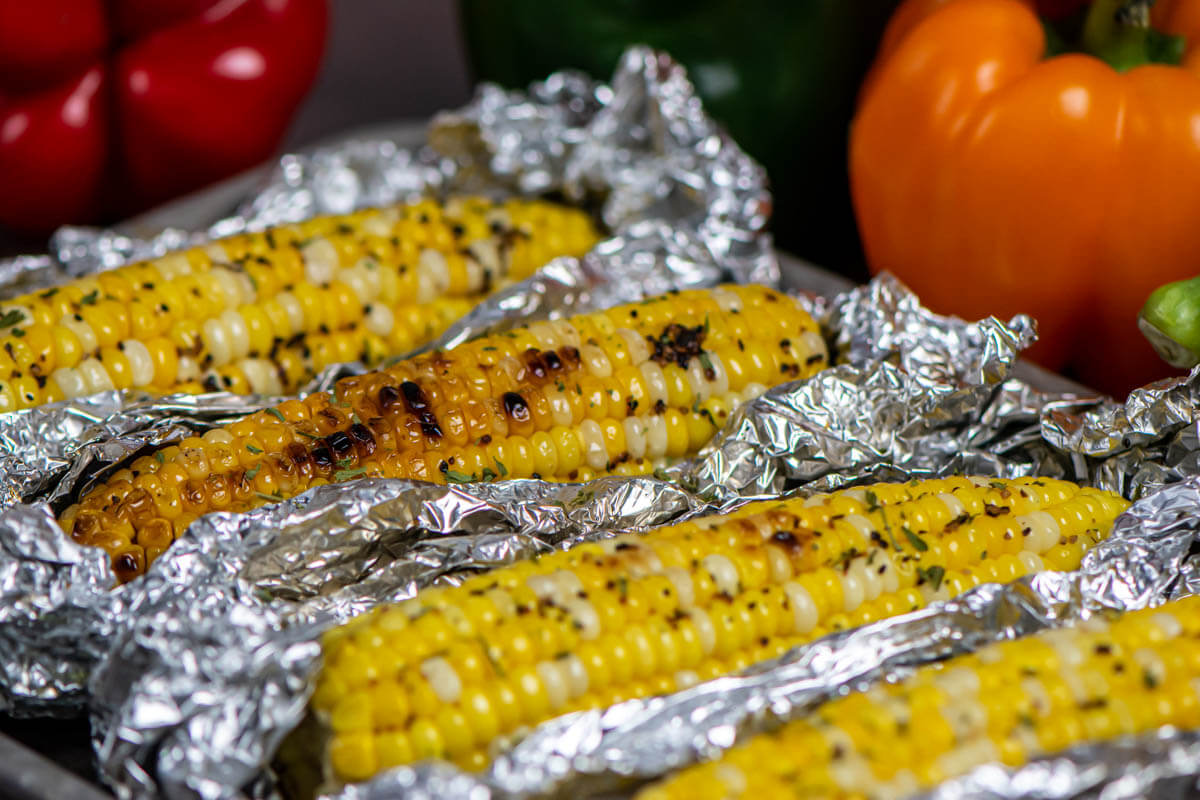 tablescape with several ears of corn resting in foil with fresh vegetables in the background.