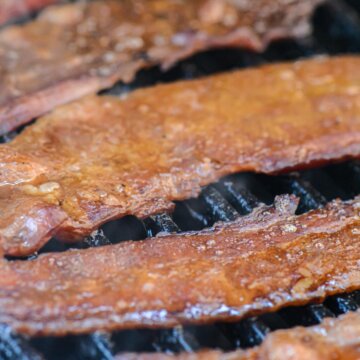 several smoked bacon slices on the cast iron grill grate after being smoked and fully cooked.