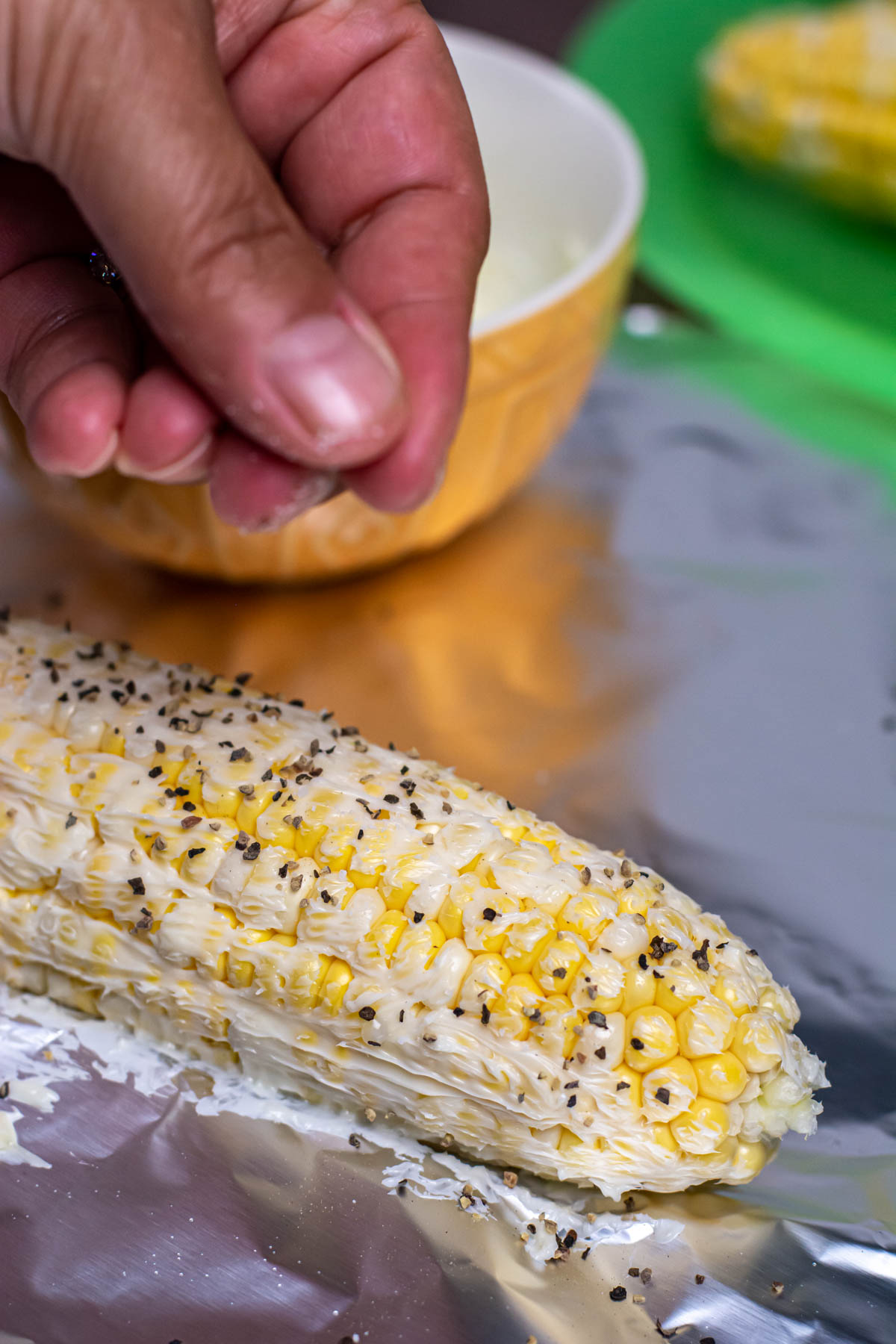 Seasoning buttered corn cobs with salt and pepper.