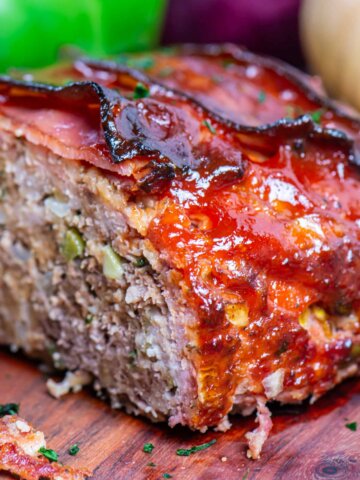 smoked meatloaf cut in half on a cutting board with vegetables in the background.