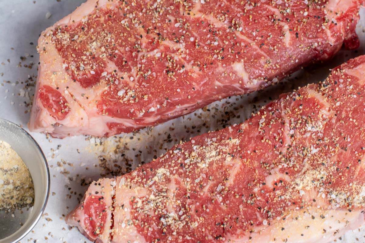 top down view of two new york strip steaks coated with salt, pepper and garlic seasonings.