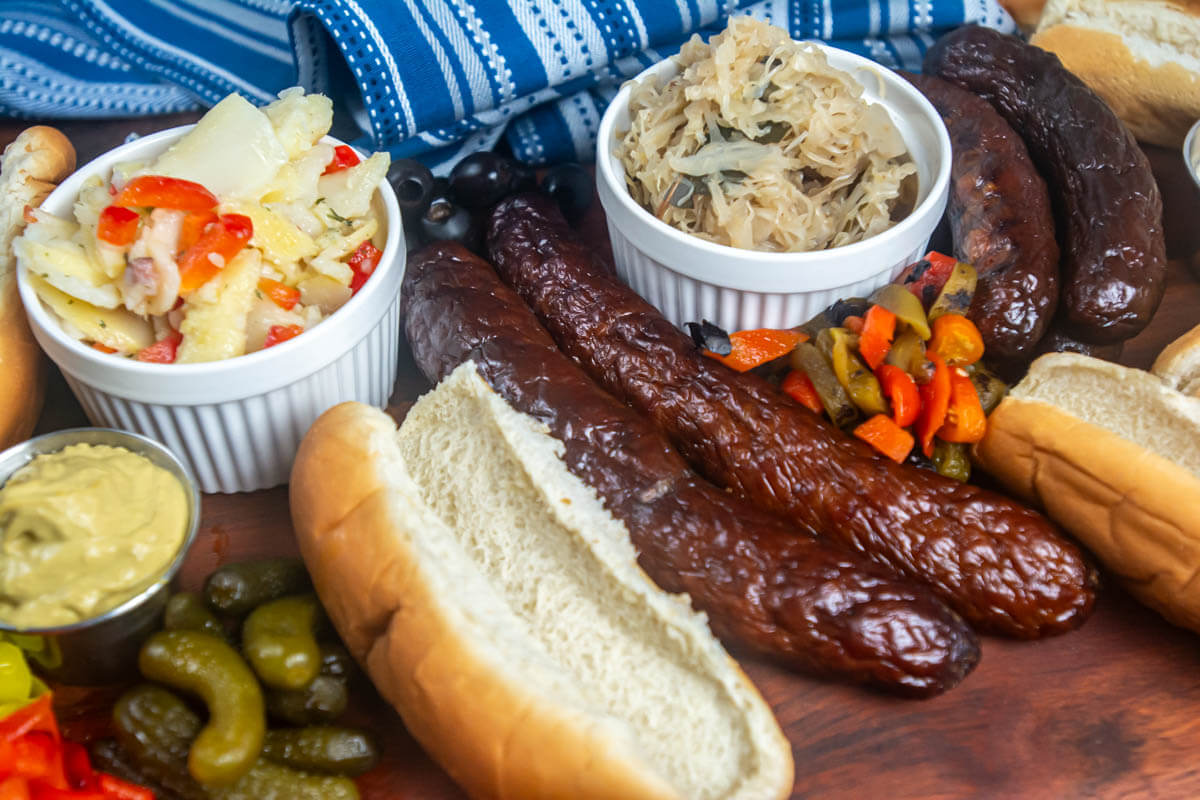 decorative table with smoked sausages, potato salad, sauerkraut, and toppings.
