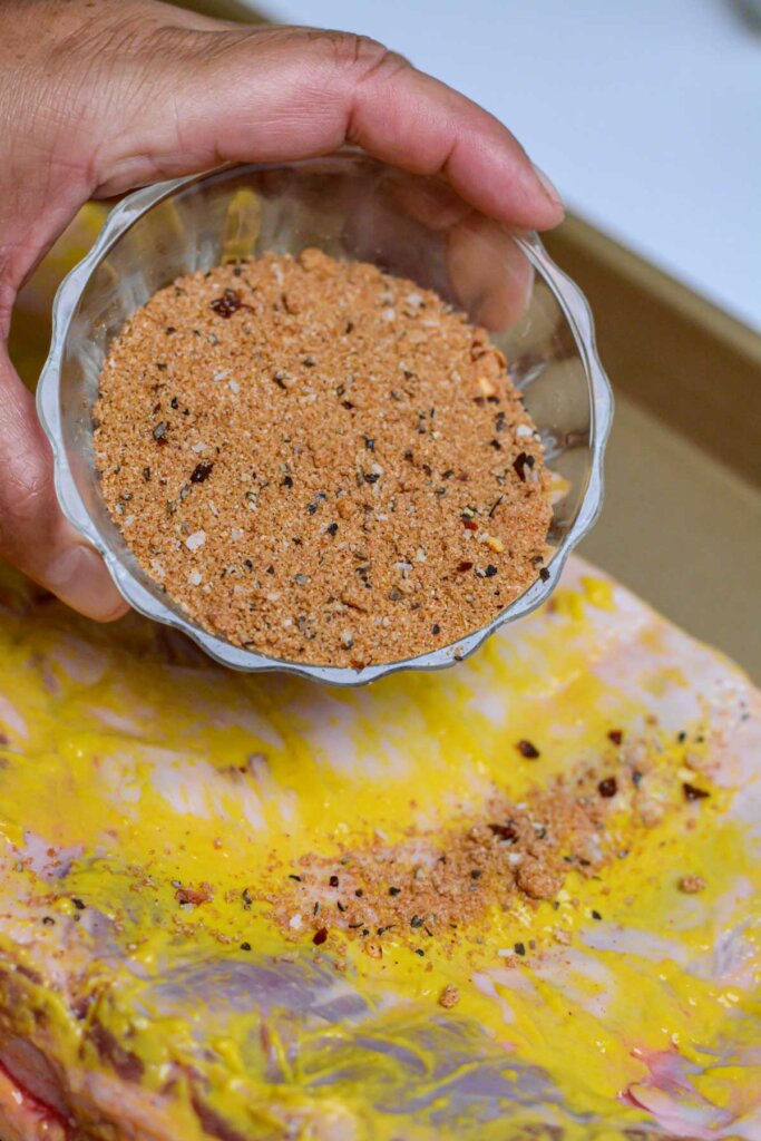 adding dry rub from a glass bowl on top of the st. louis ribs.