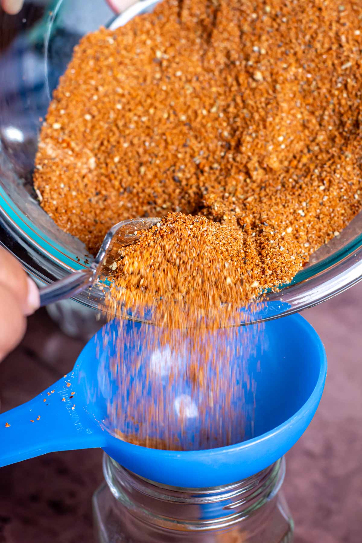 pouring the pork rub into a jar using a funnel on a decorative jar.
