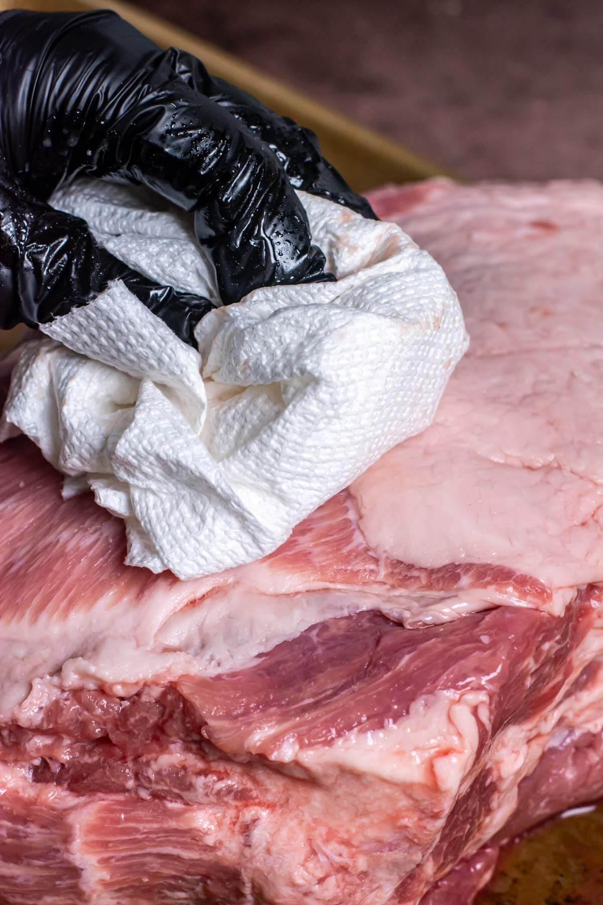 patting the pork butt dry with a paper towel on a sheet pan.