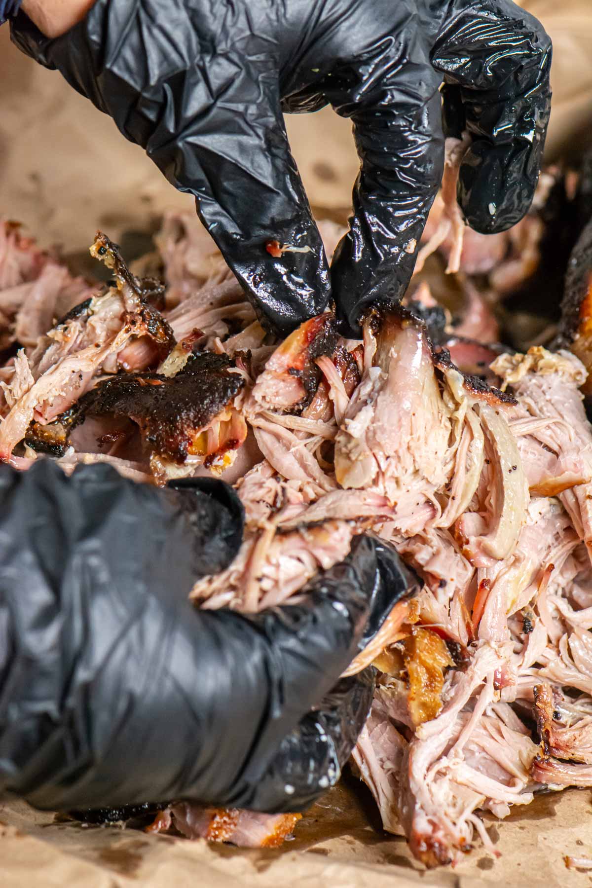 gloved hands pulling the pork from the smoked pork butt.