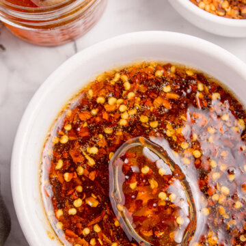 Top view of hot honey sauce with red pepper flakes in a white bowl and a spoon in it.