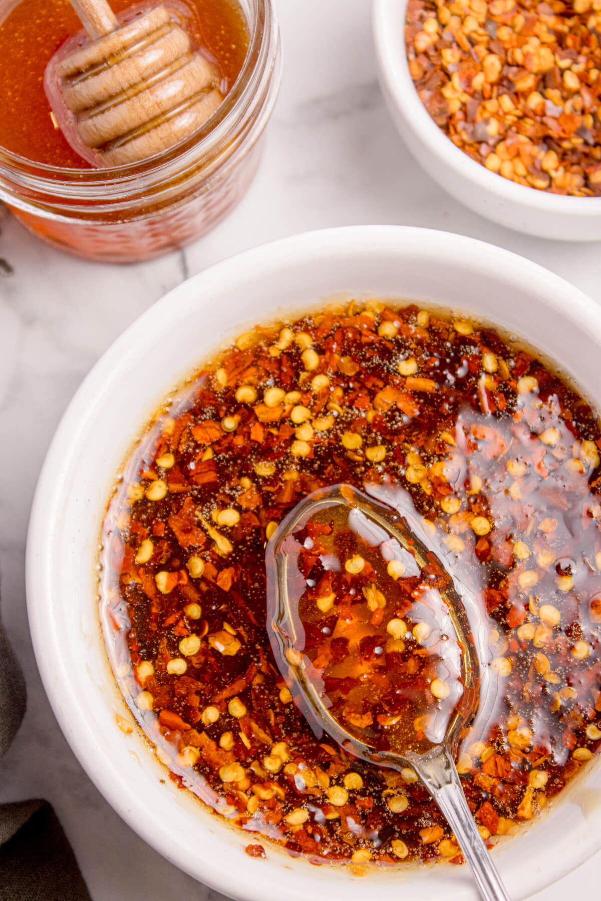 Top view of hot honey sauce with red pepper flakes in a white bowl and a spoon in it.
