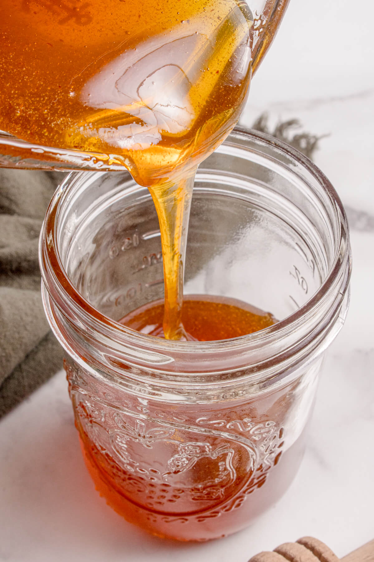 Pouring the strained and cooled hot honey into a mason jar.