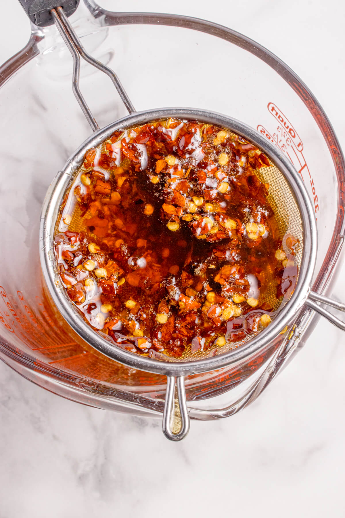 Top view of the hot honey being poured into a bowl through a strainer with the chili flakes separated.