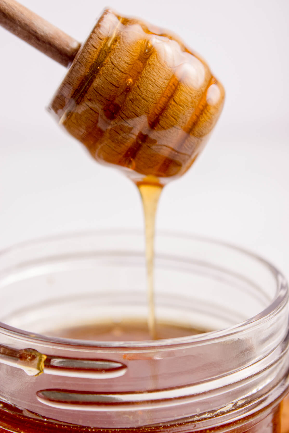 Hot honey pouring off a honey spoon in a mason jar.