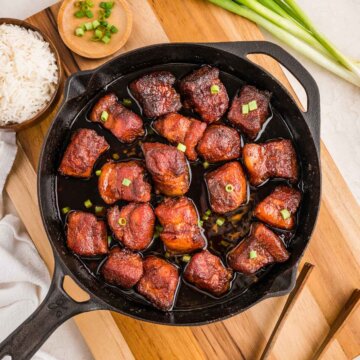 top down view of the pork belly burnt ends in a cast iron skillet with green onion and rice to accompany it.